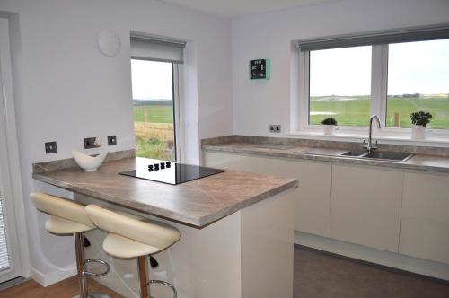 a kitchen with white cabinets and a counter with stools at Beehive Cottage in Ellon