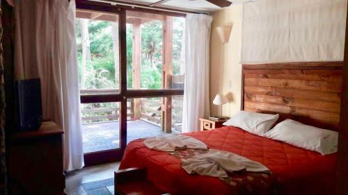 1 dormitorio con cama roja y ventana grande en Altos Medanos Cabañas & Club de Bosque en Mar de las Pampas