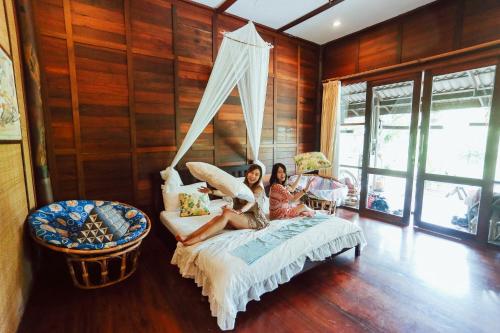 Dos mujeres sentadas en una cama en una habitación con paredes de madera en BaanSuanLeelawadee Resort Amphawa en Amphawa