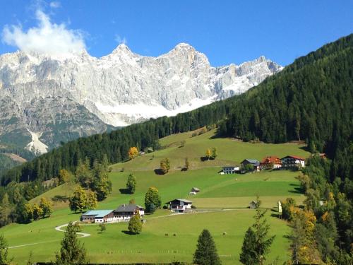 a village on a green hill with mountains in the background at Frühstückspension Rötelstein in Ramsau am Dachstein
