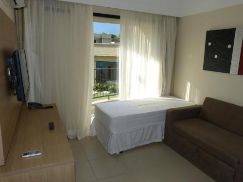 1 dormitorio con cama, sofá y ventana en Aldeia das Águas Park Resort - Flat Quartier, en Barra do Piraí
