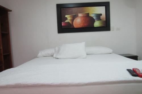 a bedroom with a white bed with a painting on the wall at Hotel Nuevo Tio in Valledupar