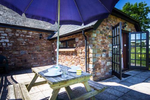 a wooden table with an umbrella on a patio at Three Gates Farm Holiday Cottages in Huntsham