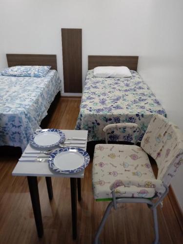 a room with two beds and a table and a chair at Mini Kitnet - Santa Cruz do Sul in Santa Cruz do Sul