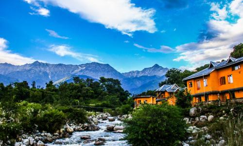 a river with houses and mountains in the background at Prakriti Aalay - Riverside Mountain View Boutique Eco Resort in Dharamshala
