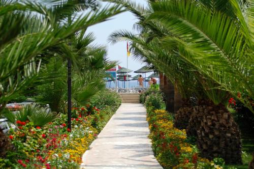 a walkway through a garden with palm trees and flowers at Kırbıyık Resort Hotel - Alanya in Kargicak