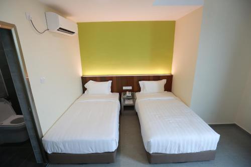 two beds in a small room with a yellow wall at Pantai Regal Boutique Hotel in Kuantan