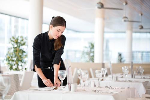 a woman is standing over a table with wine glasses at Hipotels Gran Conil in Conil de la Frontera