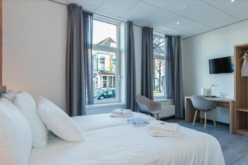 una habitación de hotel con una gran cama blanca y ventanas en City2Beach Hotel en Vlissingen