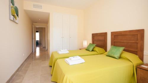 マニルバにあるDuquesa Village 14.55.12の黄色のシーツと緑の枕が備わる客室内のベッド2台