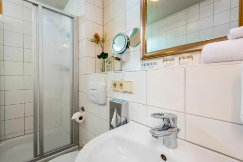 ein Bad mit einem Waschbecken, einer Dusche und einem Spiegel in der Unterkunft Hotel Ambassador-Berlin Grünau in Berlin