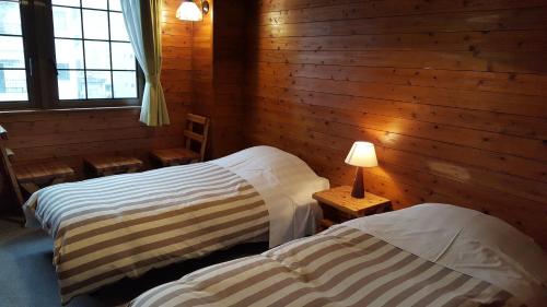 two beds in a room with wooden walls and windows at Pension Baden Heim in Nagasaki