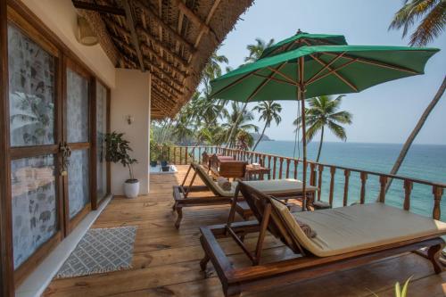 a porch with chairs and an umbrella and the ocean at The Cape Goa in Cabo de Rama