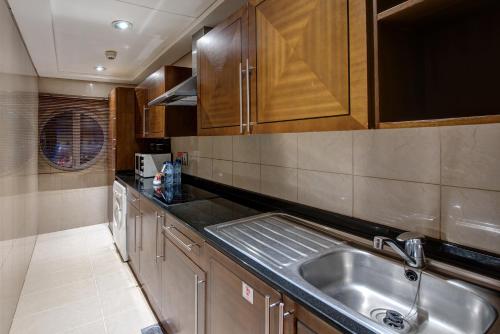 una cocina con fregadero de acero inoxidable y armarios de madera en J5 RIMAL Hotel Apartments en Dubái