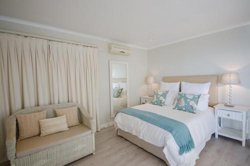a white bedroom with a bed and a chair at La Petite Baleine Seaside Villa in De Kelders