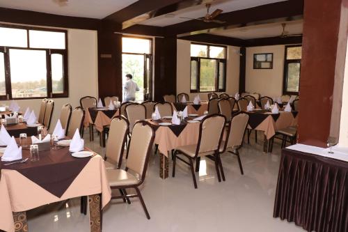 un restaurant avec des tables et des chaises et un homme debout près de la fenêtre dans l'établissement Hotel Ashiana Palampur, à Palampur