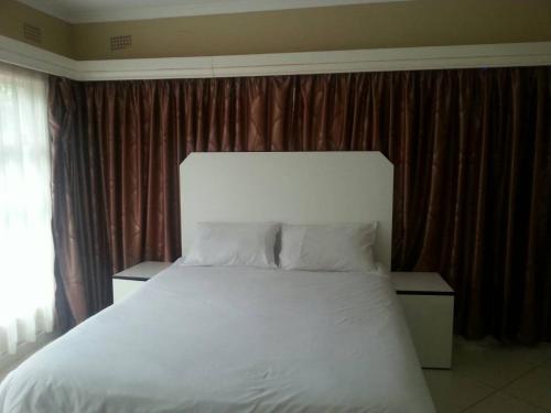Nora Valley Lodge في Ruwa: غرفة نوم بسرير ابيض كبير وستائر