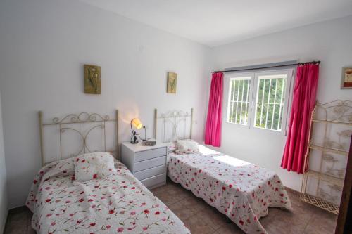 two beds in a white room with red curtains at Susana - this lovely detached holiday property in Moraira in Moraira