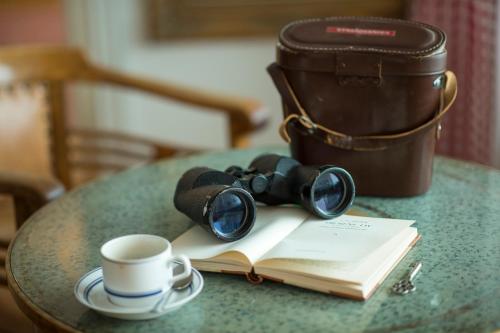 a table with a book and a cup of coffee and a pair ofoculars at Pensionat Strandgården in Mölle
