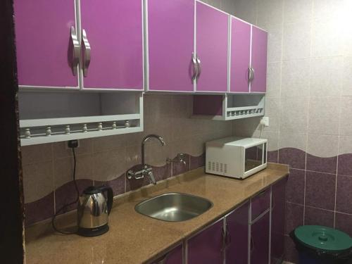eine Küche mit lila Schränken, einer Spüle und einer Mikrowelle in der Unterkunft Orchida Turaif Hotel 1 in Turaif