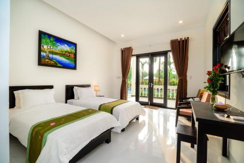 a hotel room with two beds and a desk and window at The Son Villa Hoi An in Hoi An