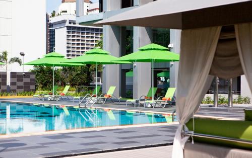 a pool with green umbrellas and chairs next to a building at Novotel Living Singapore Orchard in Singapore