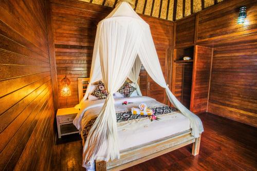 a bedroom with a bed with a mosquito net at Maha Guru Huts in Nusa Lembongan