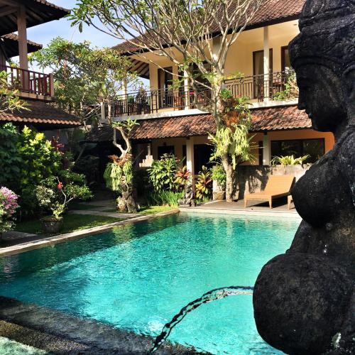 a swimming pool in front of a house with a statue at Merthayasa Bungalows in Ubud