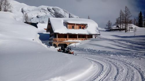 ein schneebedecktes Haus neben einer schneebedeckten Straße in der Unterkunft Lärchenhütte in Tauplitzalm