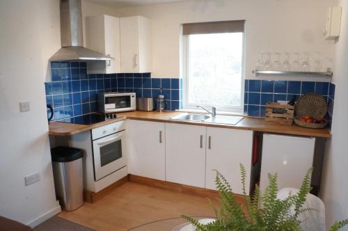 a kitchen with white cabinets and a blue tiled wall at The Oldbrook Apartment in Milton Keynes