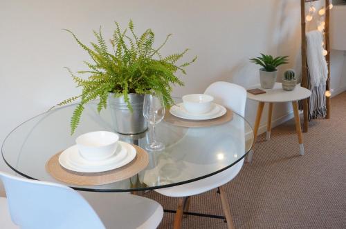 a glass table with plates and cups and a plant at The Oldbrook Apartment in Milton Keynes