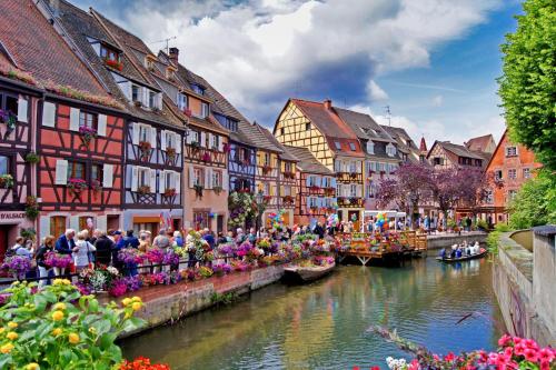 a group of people in boats on a river with buildings at camping Le Médiéval in Turckheim