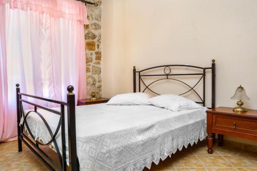 a bedroom with a bed with white sheets and pink curtains at Nireas : Stone Villa in Zakynthos