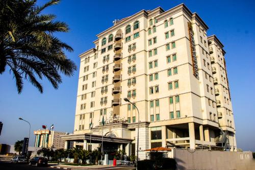 a tall white building with a palm tree in front of it at Golden Tulip Al Khobar in Al Khobar