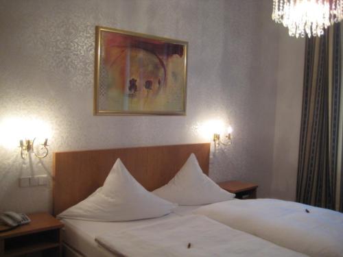 Schlafzimmer mit einem Bett mit weißer Bettwäsche und einem Kronleuchter in der Unterkunft Hotel Markgräfler Hof in Karlsruhe