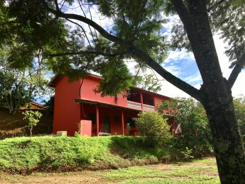 une maison rouge avec un arbre devant elle dans l'établissement Pousada Alto do Morro, à Monteiro Lobato