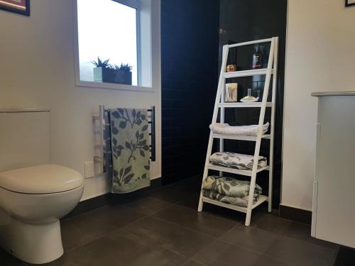 a bathroom with a toilet and a shelf with towels at House In The Heights in Taupo
