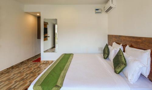 a bedroom with a bed with white sheets and green pillows at Treebo Lands End Beach Resort Morjim in Morjim