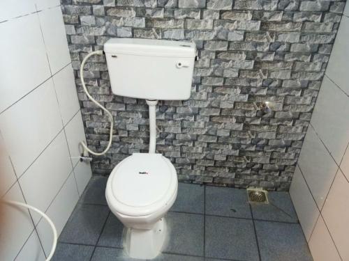a white toilet in a bathroom with a stone wall at Nook Residency in Ooty