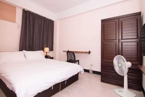 a bedroom with a white bed and a fan at 市區背包客棧 有套房可包棟 in Jincheng
