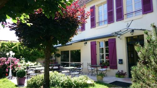 a house with purple shutters and a patio at LOGIS - Hôtel Restaurant Les Tilleuls in Saint-Florentin