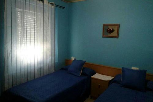 ルーゴにあるHospedaje Mendezのベッドルーム1室(ベッド2台付)、青い壁の窓が備わります。