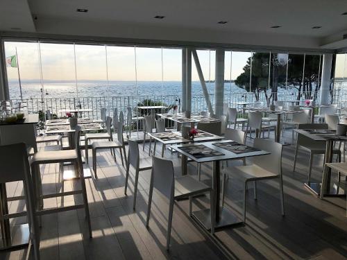 un restaurante con mesas blancas, sillas blancas y ventanas en Hotel Ca' Serena, en Sirmione
