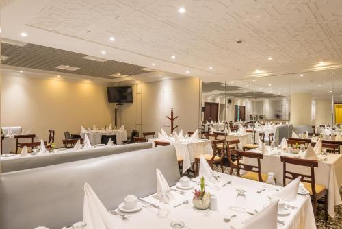um restaurante com mesas e cadeiras brancas e um espelho em Hotel Dann Av. 19 em Bogotá