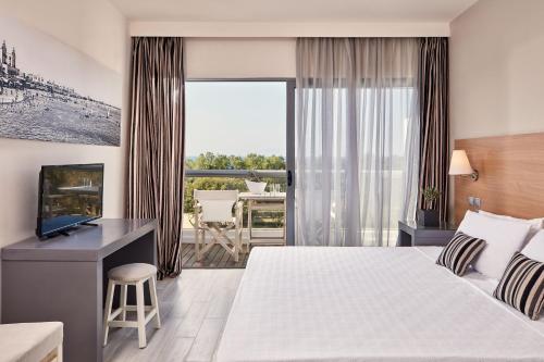 a hotel room with a bed and a television and a balcony at All Senses Ocean Blue Sea Side Resort & Spa By Anayia All Inclusive Resorts in Kremasti