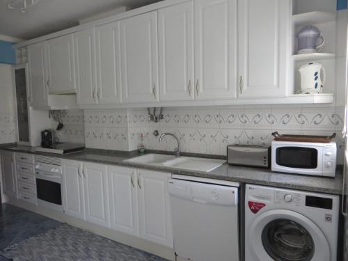 a kitchen with white cabinets and a sink and a microwave at Casa de Férias Sesimbra in Sesimbra