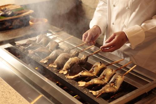 a chef cooking food on a grill with chopsticks at Minakami Hotel Juraku in Minakami