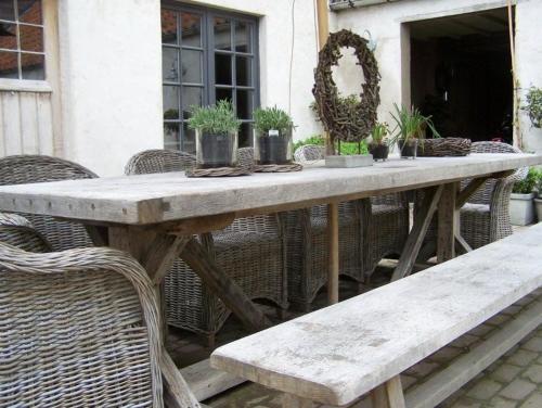 a wooden table with wicker chairs and a bench at B&B Hoeve de Steenoven in Damme