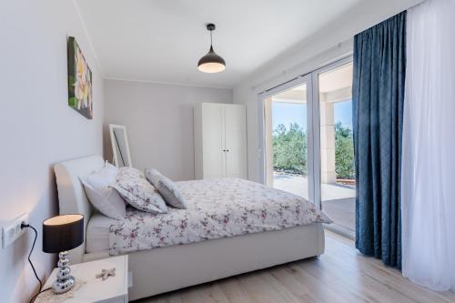 a white bedroom with a bed and a large window at The Olive Tree Villa in Sumartin