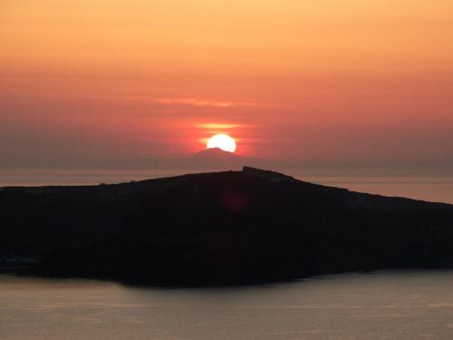 a sunset over a island in the ocean at Yposkafo Suites - Studio - Santorini in Fira